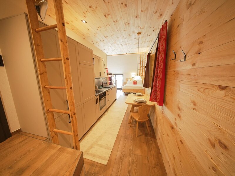 Wohn- und Schlafbereich im Bauernhof mit integrierter Küche, Esstisch und Leiter zum Hochbett.