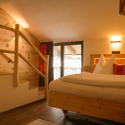 Schlafzimmer im Bauernhof mit Holzbett, Holzwänden, Treppe zu einer Empore und Balkonzugang.