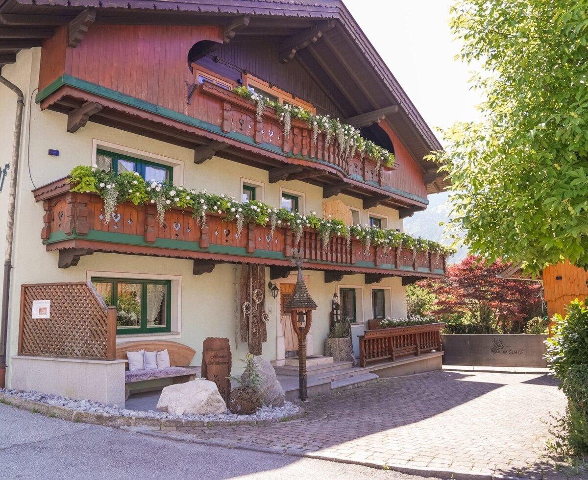 Der Bauernhof von außen mit blumengeschmückten Balkonen und einem Sitzbereich am Eingang.