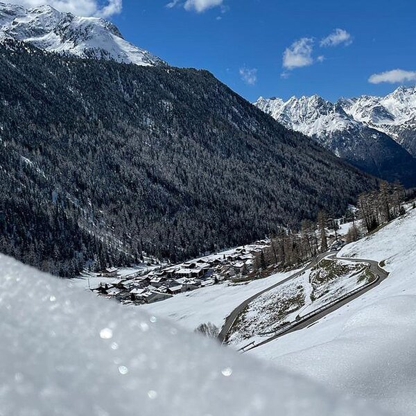 Die schneebedeckte Berglandschaft rund um den Bauernhof, mit einem Dorf im Tal und einer kurvigen Zufahrtsstraße.