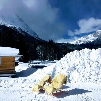 Einladende Liegestühle mit kuscheligen Fellauflagen im Schnee vor den Appartements, umgeben von einer malerischen, verschneiten Bergkulisse.
