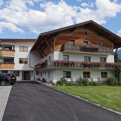 Die Außenansicht des Bauernhofs mit blumengeschmückten Balkonen und dem Gästeparkplatz.