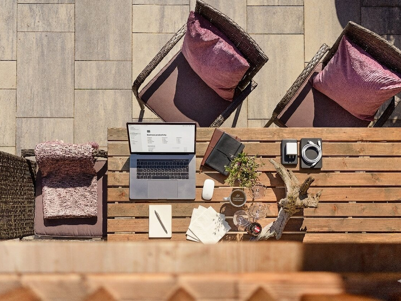 Terrasse des Bauernhofs mit einem Holztisch, Laptop, Notizbuch und Sitzgelegenheiten.