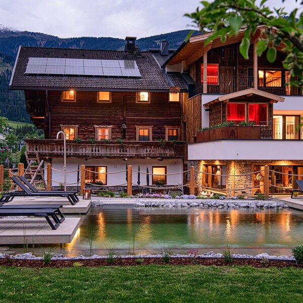 Der Bauernhof mit Naturpool und Liegestühlen im Garten, umgeben von der Berglandschaft.