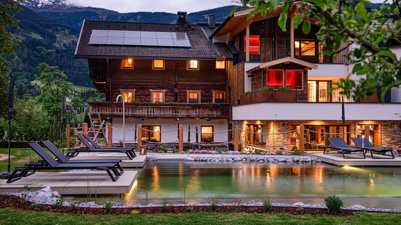 Der Bauernhof mit Naturpool und Liegestühlen im Garten, umgeben von der Berglandschaft.