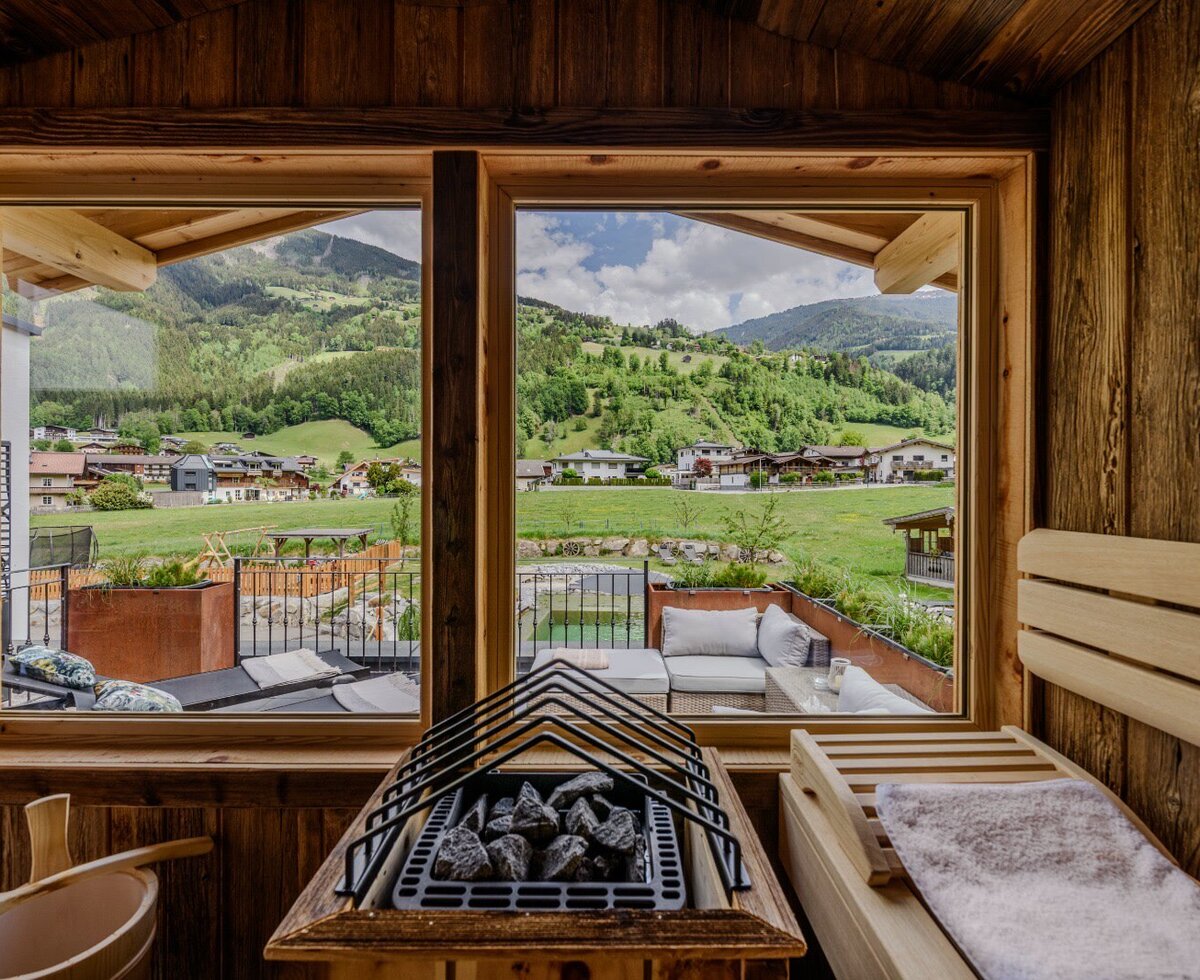 Sauna im Bauernhof mit Holzinterieur, Saunaofen und Blick auf die Berge und das Dorf.