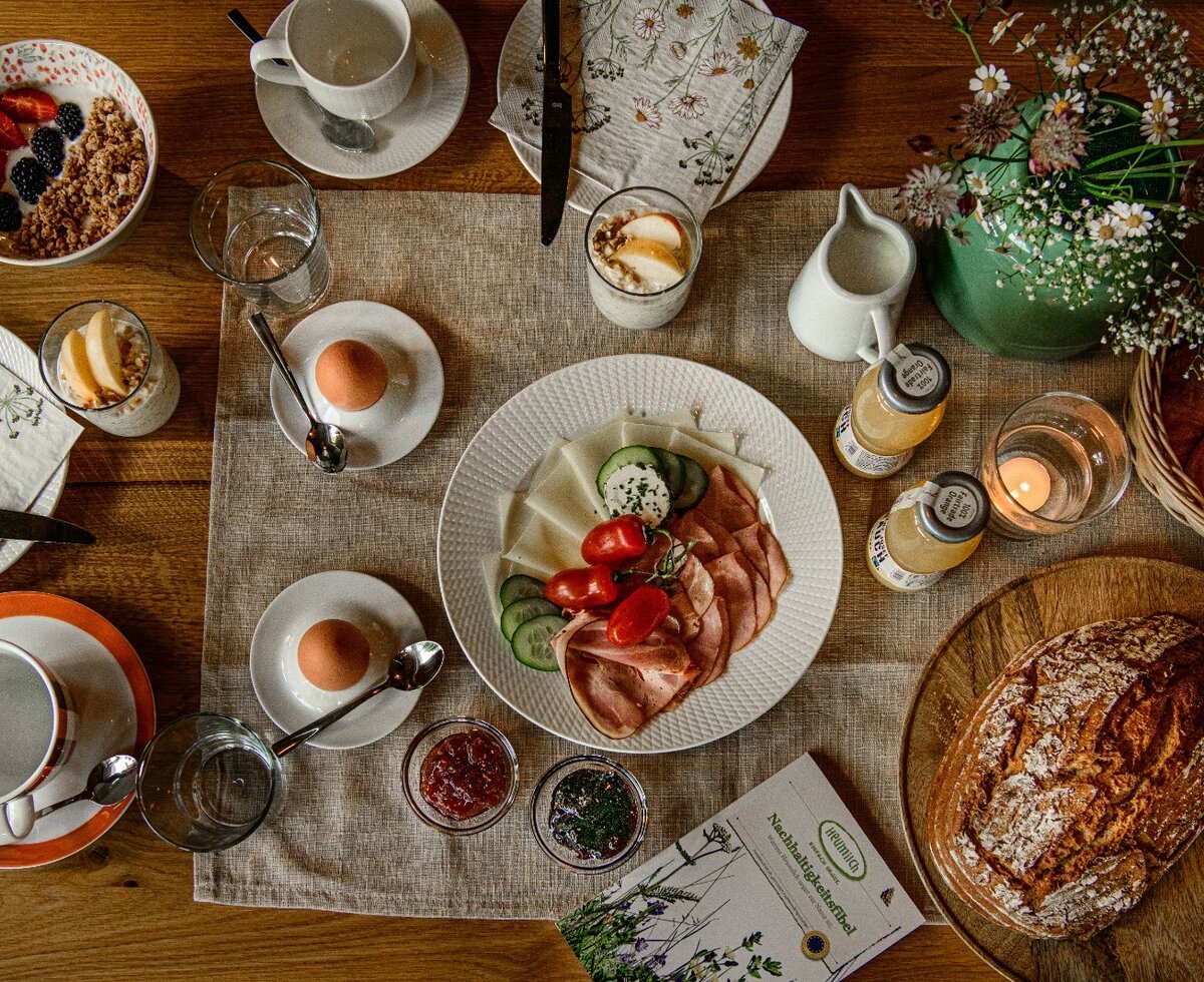 Frühstückstisch auf dem Bauernhof mit Eiern, Aufschnitt, Käse, Müsli, Brot und Getränken.