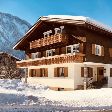 Der Bauernhof im Winter, mit zwei Balkonen und Blick auf die verschneiten Berge.