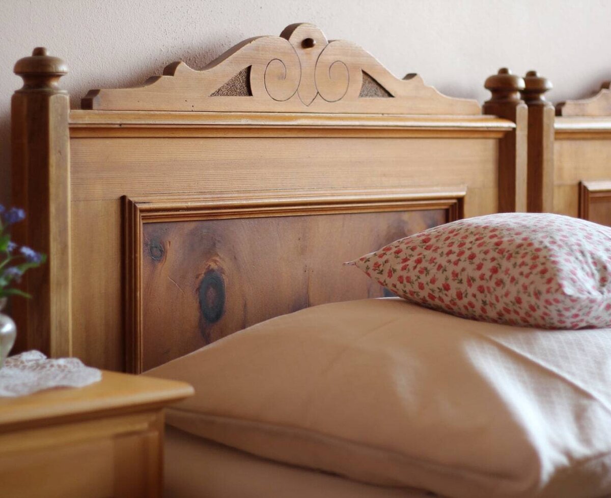 Schlafzimmer im Bauernhof mit einem Holzbettgestell, von Schwarzenberger Schreinern aus natürlichen Materialien gefertigt, und einem Nachttisch mit frischen Blumen.