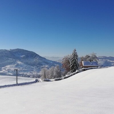 Die verschneite Winterlandschaft vom Hof in Alleinlage mit Bergen im Hintergrund, einem Gebäude und einer Skiliftstange.