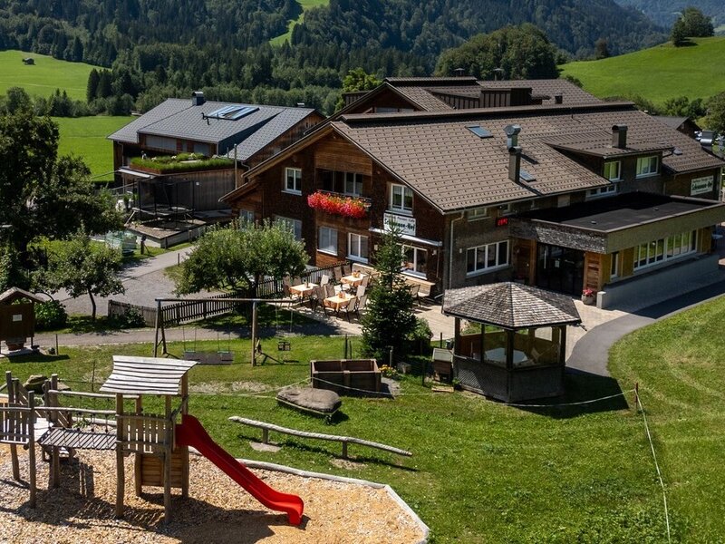 Der einladende Bauernhof mit einem weitläufigen Garten, einem Pavillon und einem abwechslungsreichen Kinderspielplatz vor saftigen grünen Wiesen.