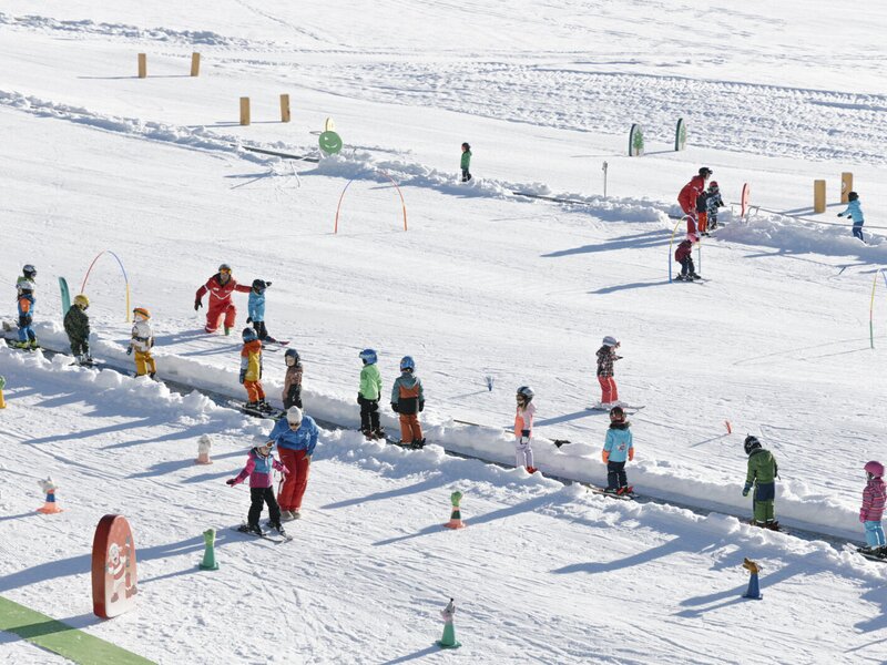 Die sonnige Kinderskischule in der Nähe des Bauernhofs mit Zauberteppichen und bunten Hindernissen für die kleinen Gäste.
