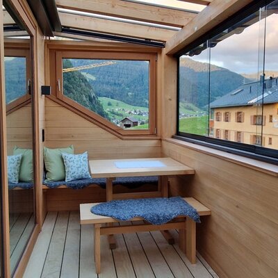 Der verglaste Balkon des Bauernhofs mit Holzeinrichtung, Esstisch und Bergblick auf die umliegende Landschaft.