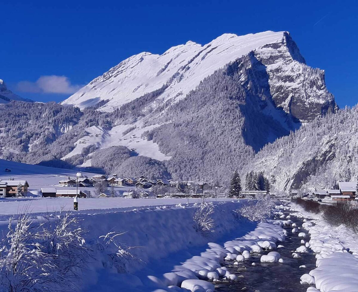 Die winterliche Umgebung des Bauernhofs mit schneebedeckten Bergen, einem Dorf und einem Fluss.