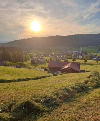 Blick über die grünen Felder auf den Bauernhof und das Dorf im Tal bei Sonnenuntergang.