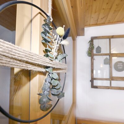 Details der Raumgestaltung in der Ferienwohnung des Bauernhofs, darunter ein Dekoring aus Seil und Trockenblumen sowie ein dekorativer Holzrahmen an der Wand.