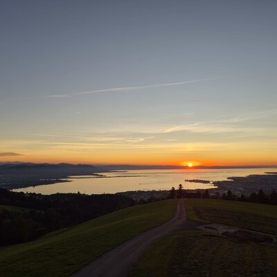 Malerischer Ausblick vom Bauernhof auf den schimmernden See und die Berge bei Sonnenuntergang.