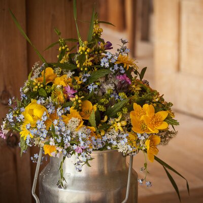 Ein Strauß Wildblumen in einer traditionellen Milchkanne auf dem Bauernhof.
