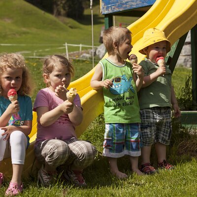 Spielplatz auf dem Bauernhof mit einer gelben Rutsche und Kindern, die Eis essen.