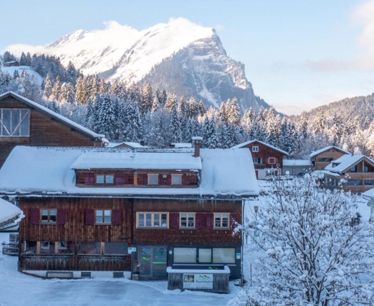 Der verschneite Bauernhof mit seinen traditionellen Gebäuden vor der Kulisse einer winterlichen Berglandschaft.
