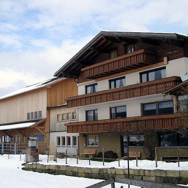 Außenansicht des Bauernhofs mit mehreren Balkonen und angrenzendem Holzgebäude im Winter.