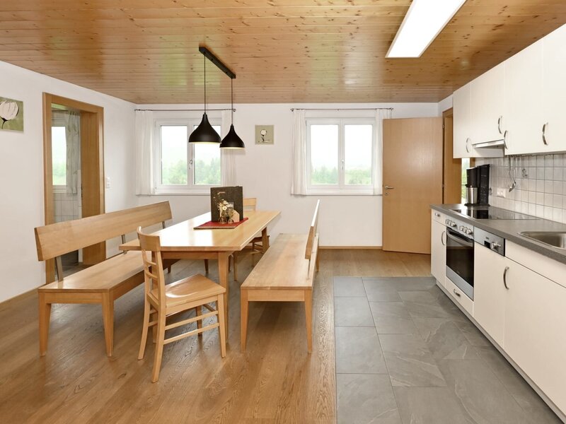 Die Wohnküche der Ferienwohnung auf dem Bauernhof mit Esstisch, Bänken und einer voll ausgestatteten Küche inklusive Geschirrspülmaschine und Backofen.