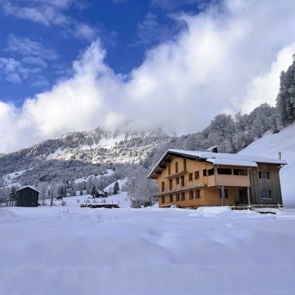 Das Wohnhaus mit Holzfassade und Balkonen, eingebettet in eine verschneite Berglandschaft.