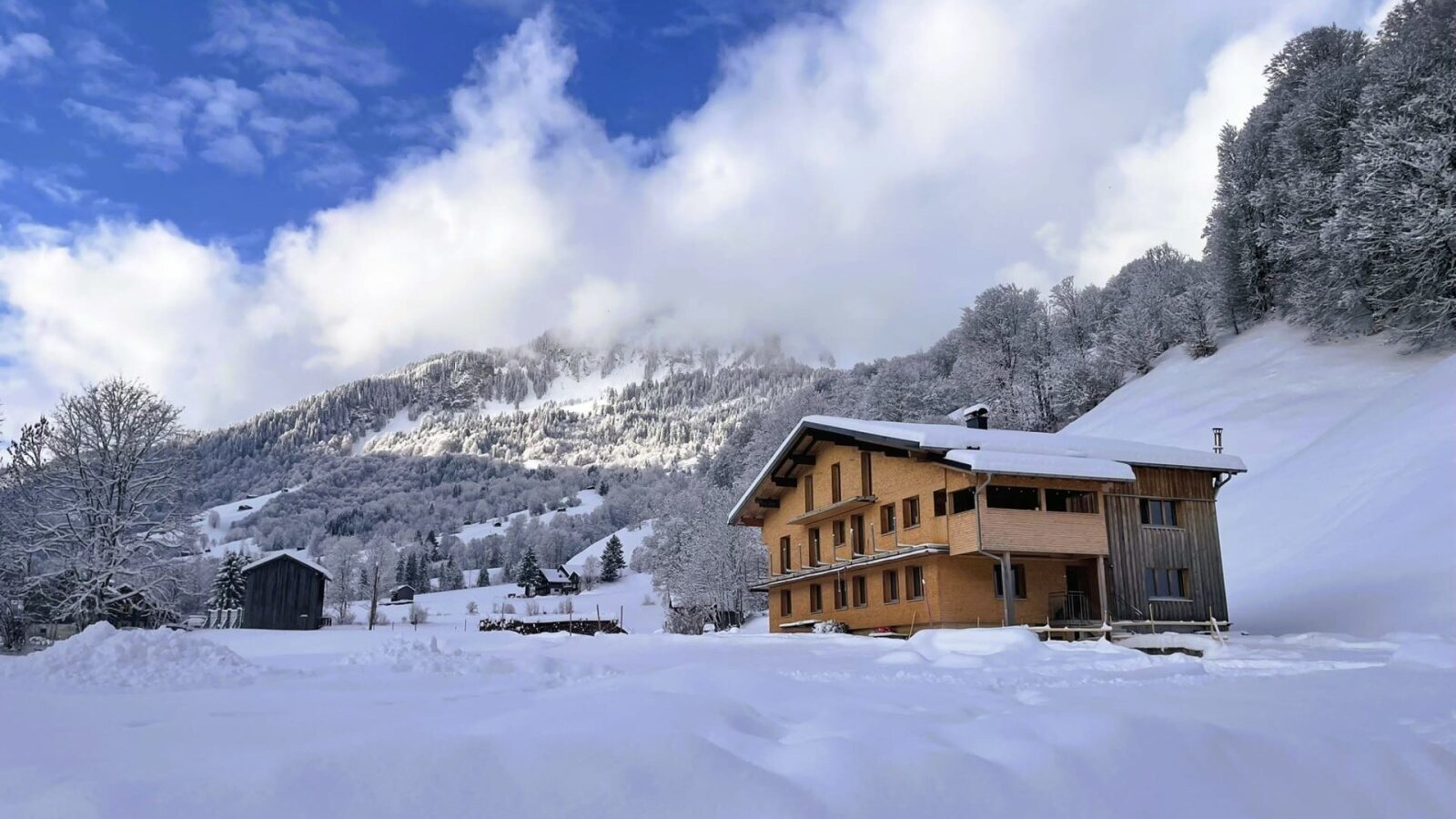 Das Wohnhaus mit Holzfassade und Balkonen, eingebettet in eine verschneite Berglandschaft.