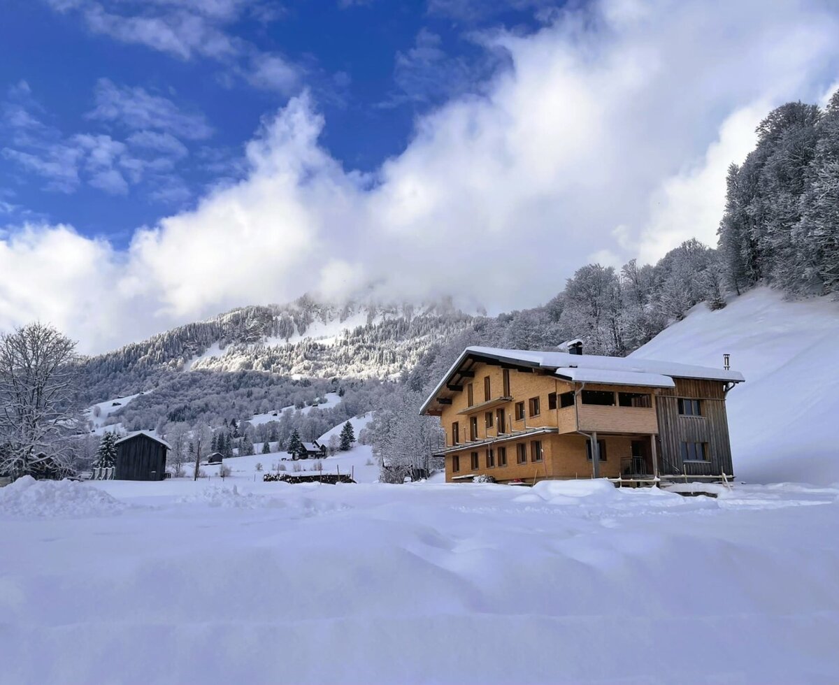 Das Wohnhaus mit Holzfassade und Balkonen, eingebettet in eine verschneite Berglandschaft.