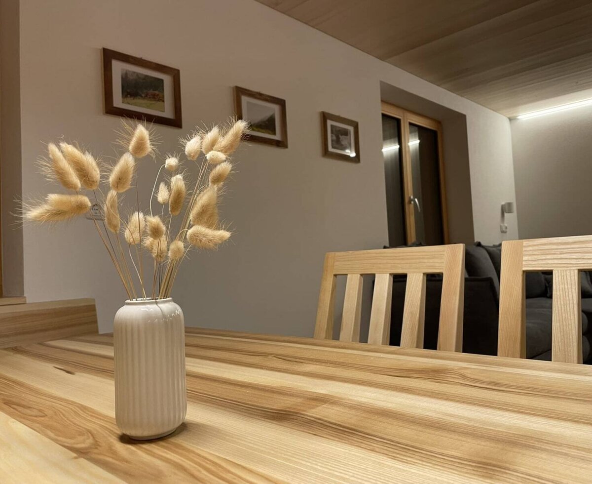 Holz-Esstisch in der Ferienwohnung mit Vase, Stühlen und einem Sofa im Hintergrund.