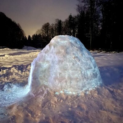 Ein stimmungsvoll beleuchtetes Iglu im verschneiten Außenbereich der Ferienwohnung bei Nacht.