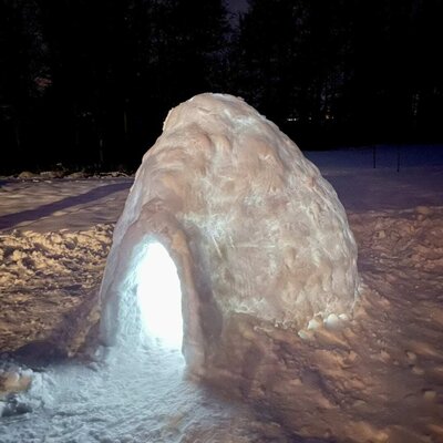 Ein stimmungsvoll beleuchtetes Iglu im verschneiten Außenbereich der Ferienwohnung bei Nacht.