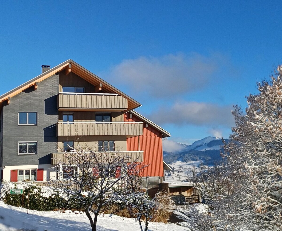 Der Bauernhof in einer verschneiten Landschaft und mit Blick auf die Berge.