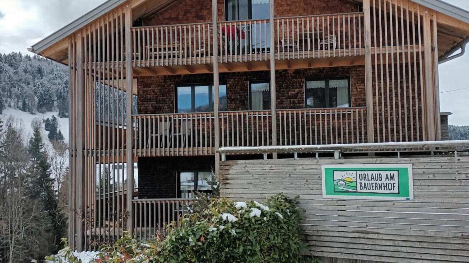 Das Bauernhof-Gebäude mit Holzfassade, Balkonen und winterlicher Umgebung.