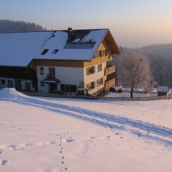 Der Bauernhof im Winter, mit verschneitem Dach, Solarpaneelen und umgeben von einer schneebedeckten Landschaft.