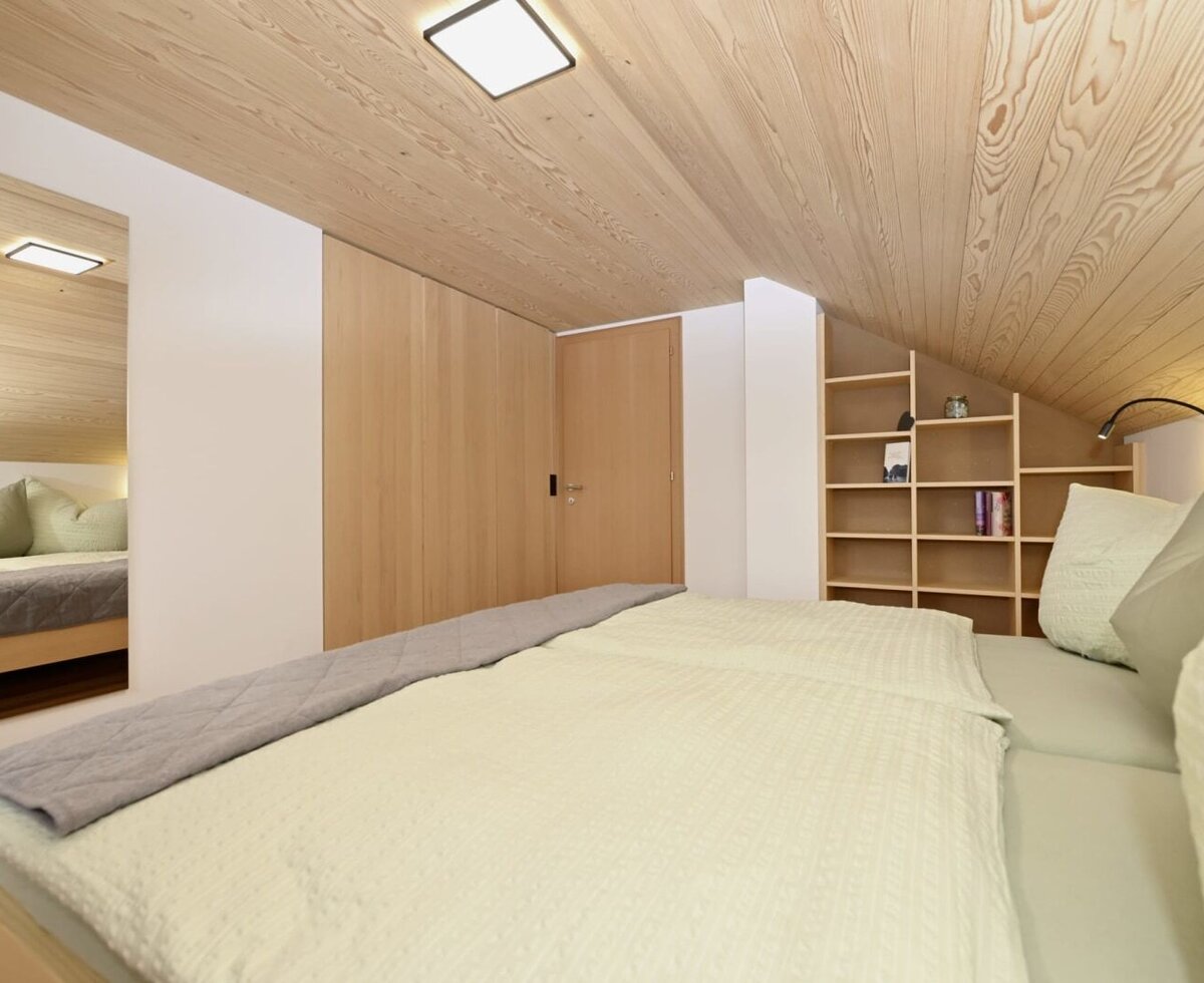 Schlafzimmer mit großem Bett, Holzdecke, Einbauschränken und Regal.