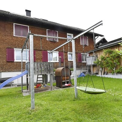 Kinderspielplatz im Garten des Bauernhofs mit Rutsche, Schaukeln und Sandkasten.