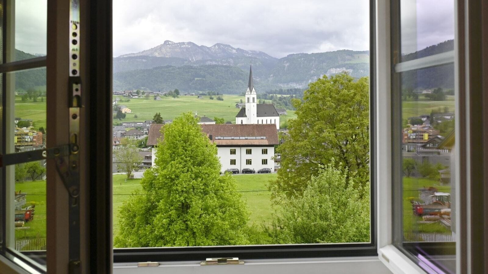 Blick aus dem Fenster auf das Dorf mit Kirche und die umliegende Berglandschaft.