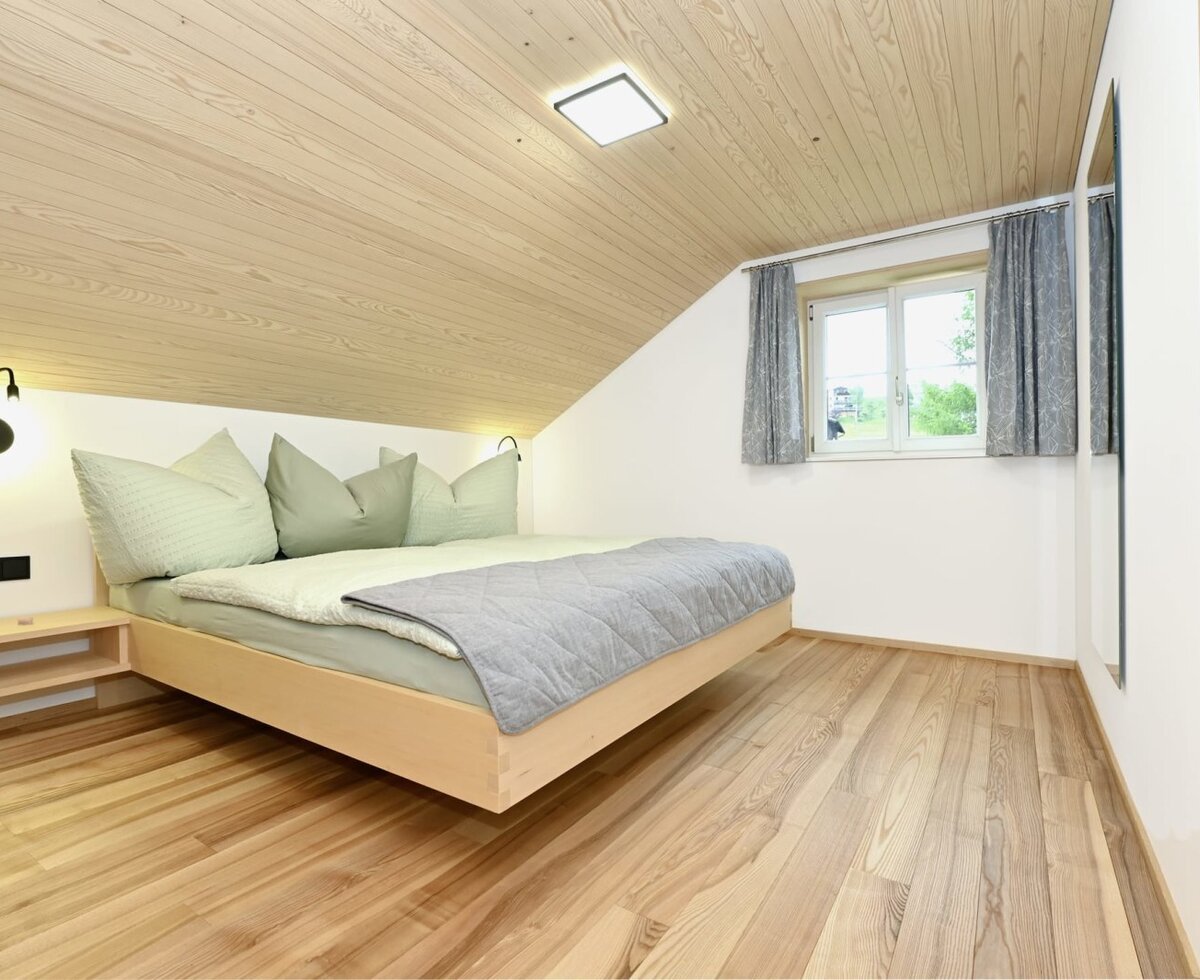 Schlafzimmer mit Doppelbett, Holzverkleidung an der Dachschräge und Holzboden.