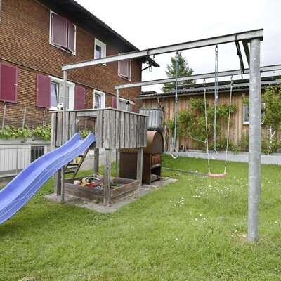 Der Kinderspielplatz am Hof mit Rutsche, Sandkasten und Schaukeln.