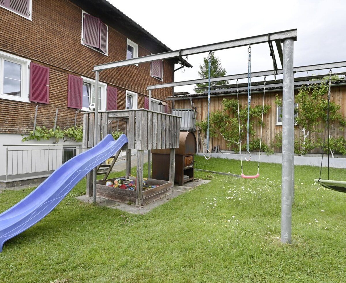 Der Kinderspielplatz am Hof mit Rutsche, Sandkasten und Schaukeln.