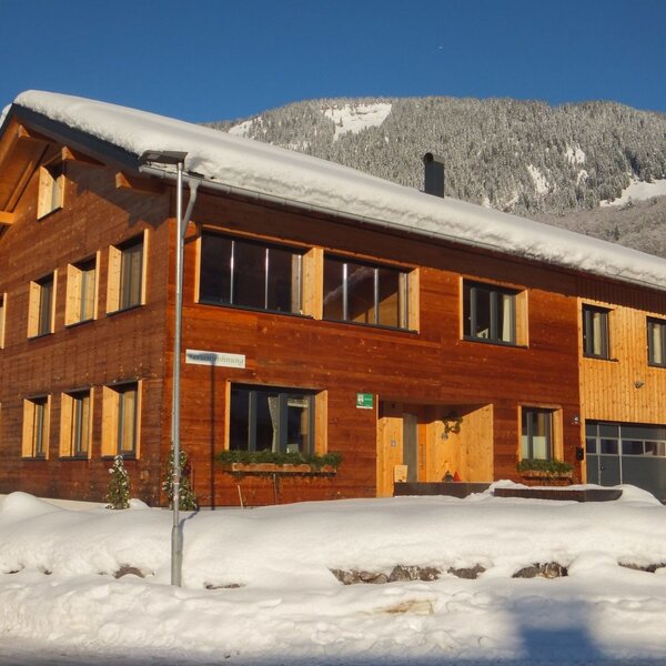 Der neu erbaute Bauernhof aus Vollholz, umgeben von Schnee im Winter, mit einer Bergkulisse im Hintergrund.