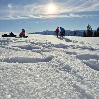 Eine Familie genießt eine Winterwanderung im Schnee mit Bergblick vom Bauernhof aus.
